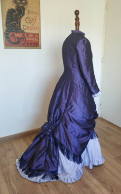 Outfit naar het model van een 'polonaise dress' uit ongeveer 1870. De donkerpaarse overjurk en lichtpaarse rok zijn van taftzijde. Gedragen over een zelfgemaakte petticoat. Victoriaanse polonaise jurk