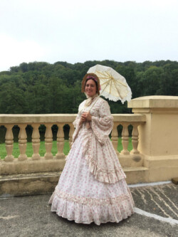 Zomerjurk naar authentiek model van rond 1865. Rok en lijfje gemaakt van zeer dunne katoen, gedragen over een zelfgemaakt korset, petticoat en hoepelrok. Ook de parasol en hoed zijn zelfgemaakt. Victoriaanse zomerjurk