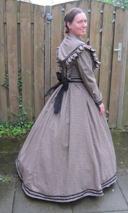 Wollen jurk gebaseerd op een model uit ongeveer 1865, gedragen over een ook zelfgemaakt korset, petticoat en hoepelrok. Victoriaanse reisjurk