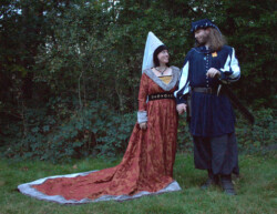 Jurk met hoed gebaseerd op een middeleeuwse houppelande, en blauwe tuniek met pofmouwen en 'chaperon' hoed; beide gemaakt van moderne materialen. Middeleeuws geïnspireerde kostuums
