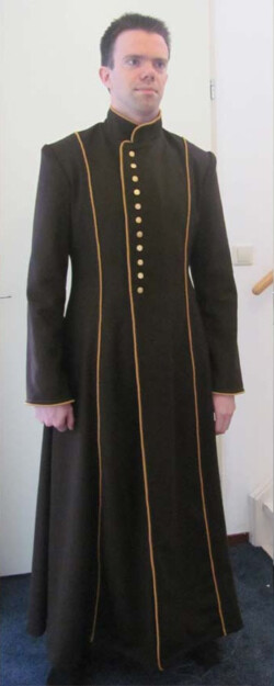 Lange bruine wollen jas met gele decoratieve bandjes en goudkleurige knopen. Fantasiejas