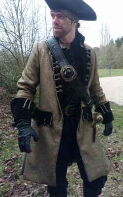 Piratenjas van goudkleurige stof, met zwarte fluwelen elementen en goudband ter afwerking. Piratenjas